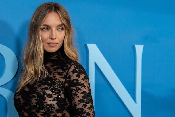 Jodie Comer trägt ein schwarzes Spitzenoberteil vor einem blauen Hintergrund.
