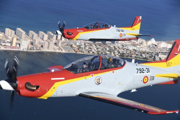 Zwei Pilatus PC-21 Schulungsflugzeuge der spanischen Luftwaffe fliegen in Formation über einer Küstenstadt.