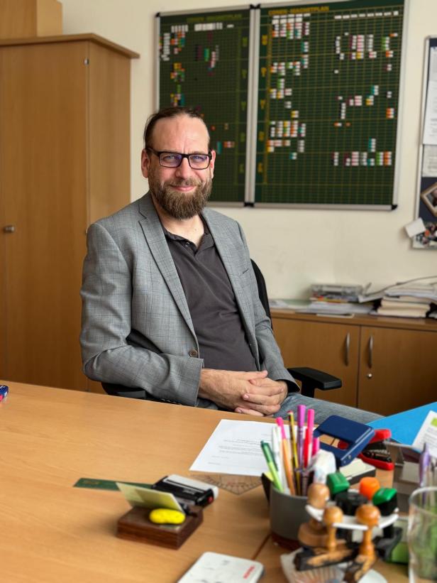 Mann mit Brille und Bart sitzt lächelnd im Büro am Schreibtisch.