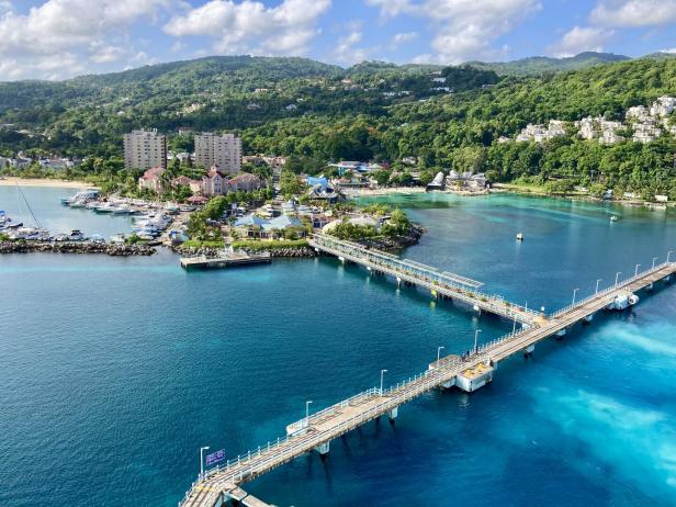 Ein langer Steg führt in Ocho Rios auf Jamaika zu einer Küstenlandschaft mit Yachthafen, Gebäuden und bewaldeten Hügeln.