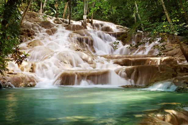 Die Dunn’s River Falls in Jamaika stürzen über terrassenförmige Felsen in ein klares, türkisfarbenes Becken inmitten eines üppigen Waldes.