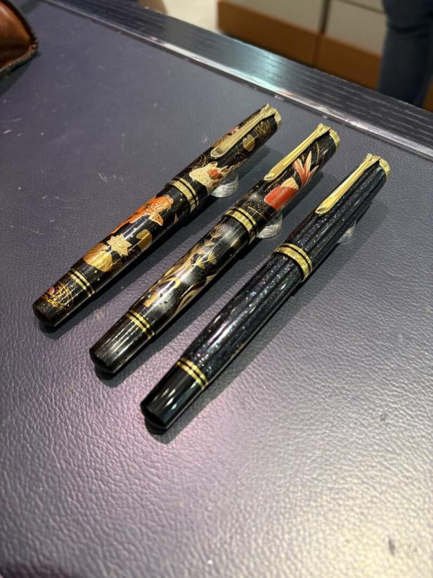 Drei schwarze Füllfederhalter mit Goldakzenten und japanischen Motiven liegen auf einer Tischfläche.