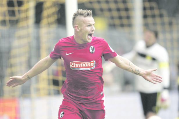 Ein Fußballspieler in rotem Trikot jubelt mit offenen Armen auf dem Spielfeld.