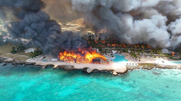 Küstenresort in Flammen, dichte Rauchwolken steigen über dem Meer auf.