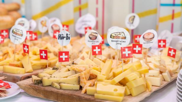 Käseauswahl auf Holzplatten mit Schweizer Fähnchen und Sortenschildern.