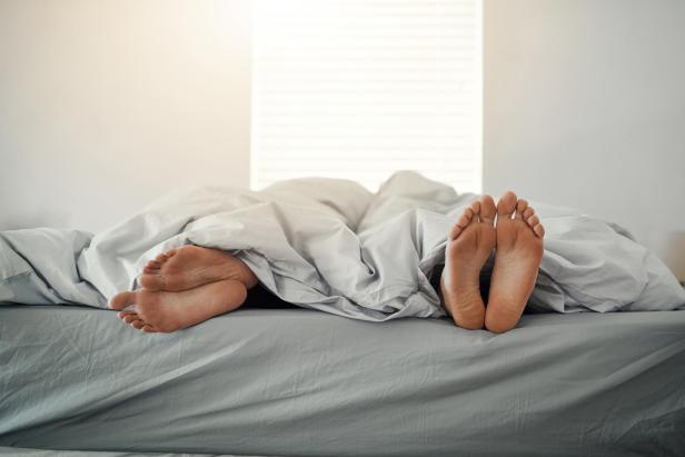 Zwei Personen schlafen im Bett, nur ihre Füße ragen unter der Decke hervor.
