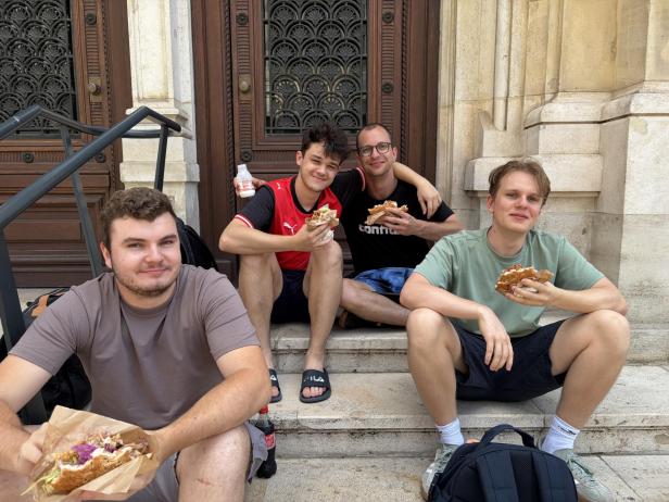 Vier Jugendliche essen einen Döner auf den Stiegen vor der Oper.