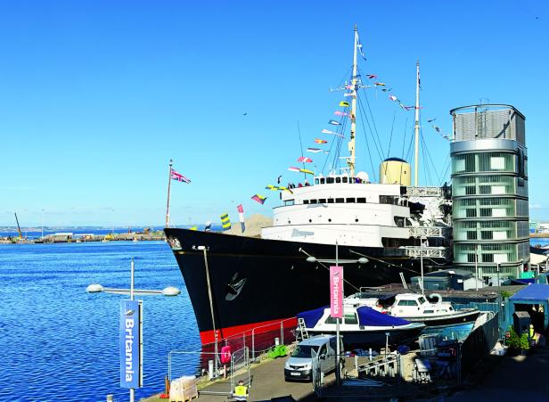 Die königliche Yacht Britannia liegt an einem Kai in Leith vor Anker, geschmückt mit Flaggen unter einem klaren blauen Himmel.