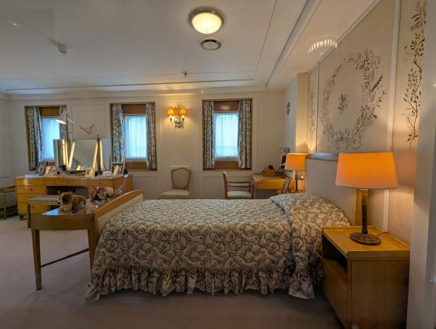 Elegantes Schlafzimmer mit Einzelbett, Schreibtisch, Spiegel, Lampen und floralen Wandmotiven.