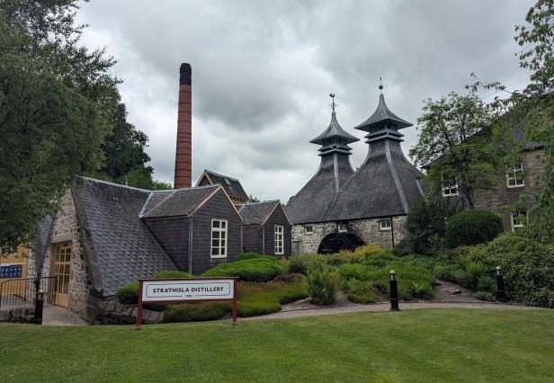 Strathisla Distillery mit historischen Gebäuden, zwei Pagodendächern und hohem Schornstein unter grauem Himmel.