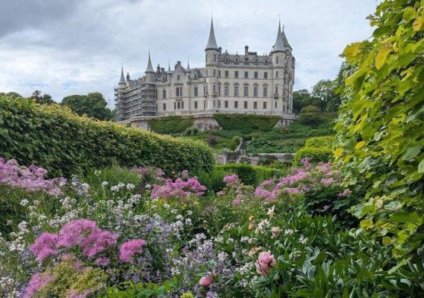 Dunrobin Castle in Schottland thront über einem farbenfrohen, blühenden Garten mit üppigen Pflanzen und Blumen.