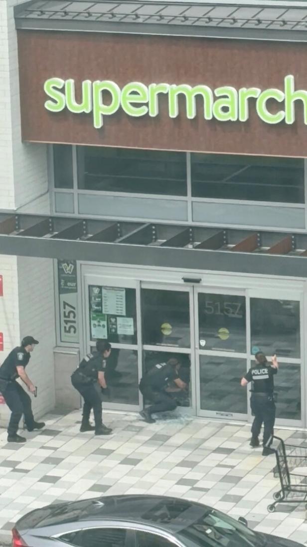 Police officers enter a supermarket through a broken window as they operate amidst a deadly shooting incident, in Montreal
