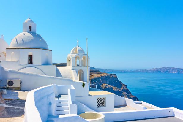 Weiße Kirche mit Kuppel vor der Steilküste und dem tiefblauen Meer auf der griechischen Insel Santorin.