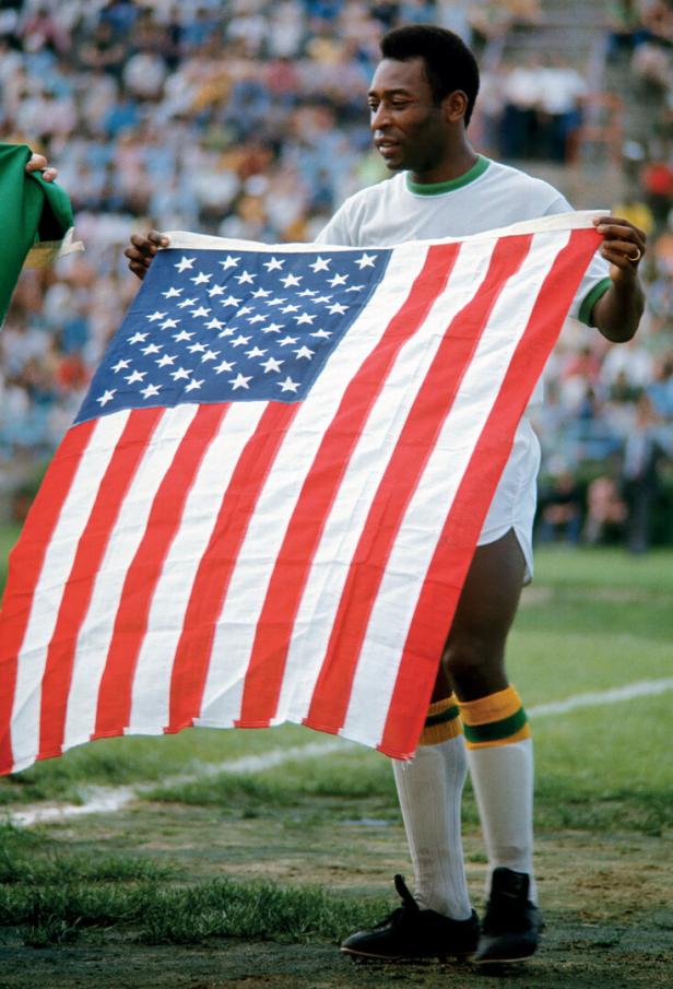 Pelé hält auf einem Fußballfeld eine US-amerikanische Flagge in die Höhe.
