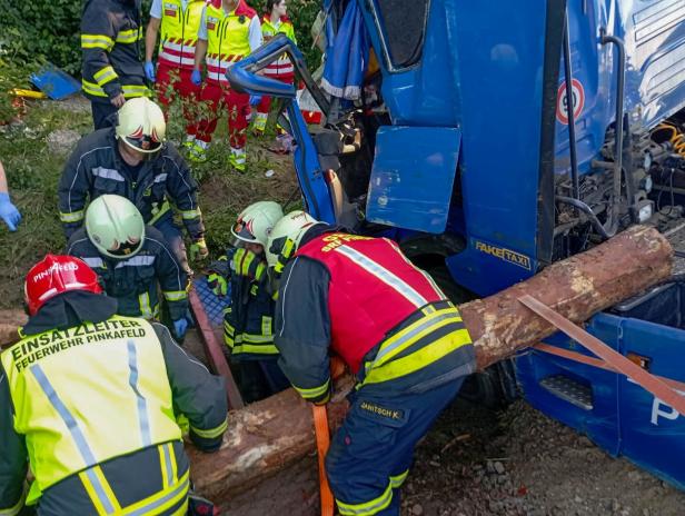 Rettungskräfte bergen mit Gurten einen Baumstamm aus einem verunglückten blauen Lkw.