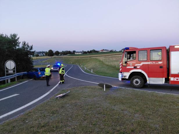 Polizei und Feuerwehr sichern einen Unfall mit einem blauen Auto am Straßenrand ab.