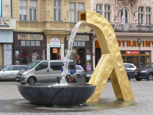 Ein goldener Brunnen auf einem belebten Platz in einer tschechischen Stadt.