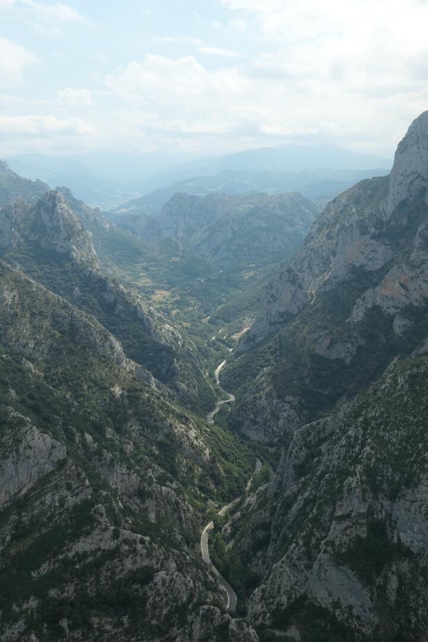 Schmale Straße windet sich durch ein tiefes, felsiges Bergtal unter bewölktem Himmel.