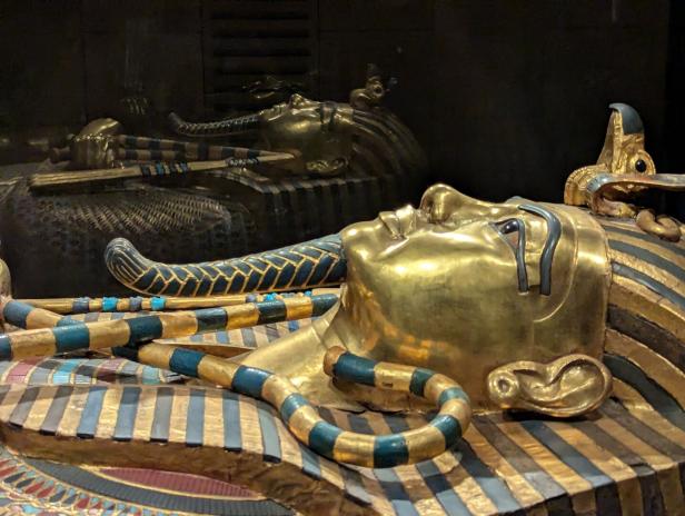 Goldene ägyptische Sarkophage mit blau-goldenen Streifen und Tierköpfen in dunkler Vitrine.