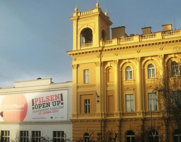 Ein gelbes Gebäude in Pilsen mit einem Werbeplakat für „Pilsen 2015“.