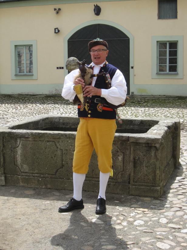 Ein Mann in Tracht spielt ein traditionelles Instrument vor einem Gebäude.
