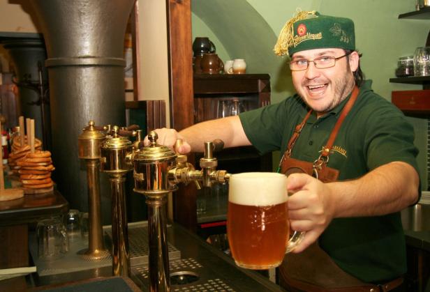 Ein Mann mit Pilsner Urquell-Mütze zapft ein Bier.