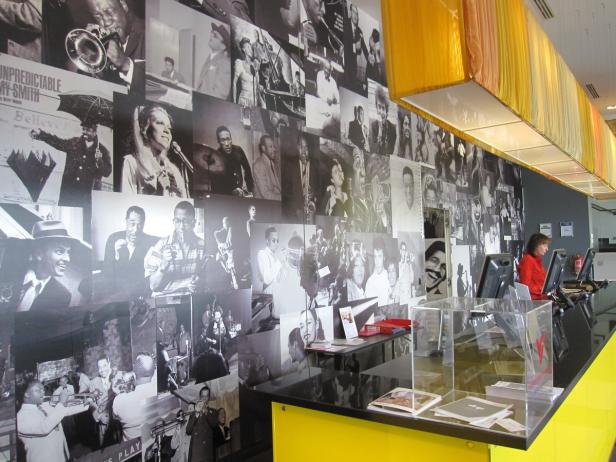 Eine Frau arbeitet an einem Schalter vor einer Wand voller Schwarz-Weiß-Fotografien von Musikern.