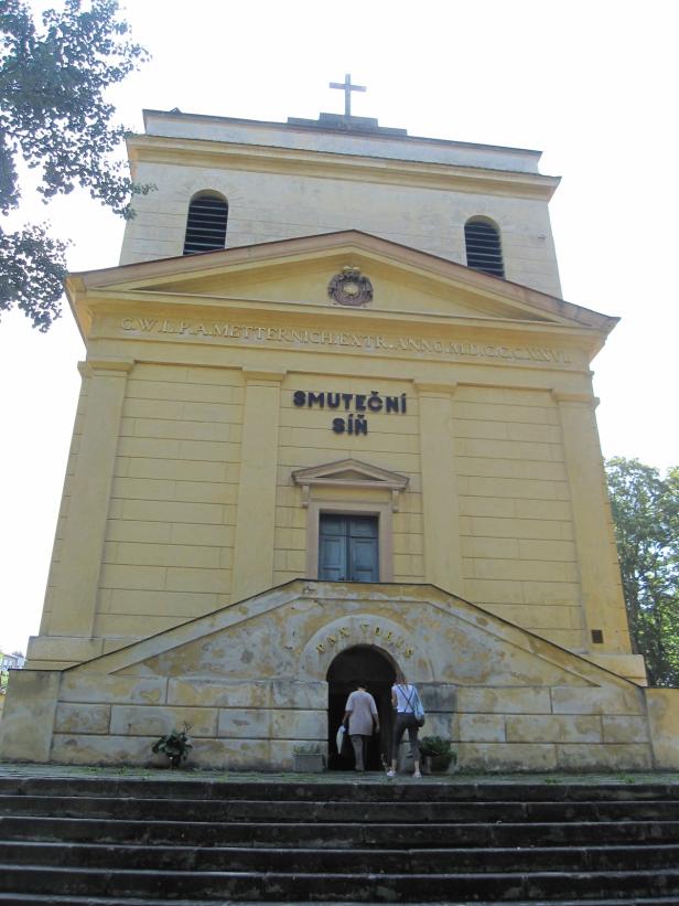 Zwei Personen betreten die „Smuteční síň“ durch einen Torbogen.