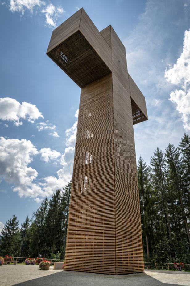 Hoher hölzerner Aussichtsturm im Wald unter blauem Himmel.