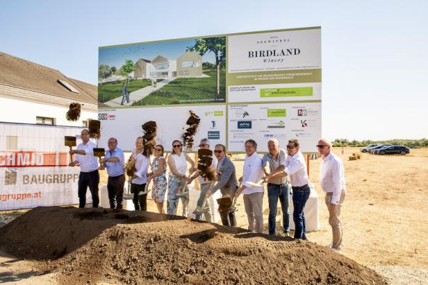 Gruppe beim Spatenstich vor einem Baustellenschild für das Birdland Winery-Projekt.