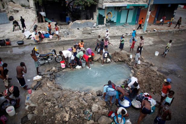 FILE PHOTO: People collect water from a broken pipe under the asphalt near the presidential palace in Port-au-Prince
