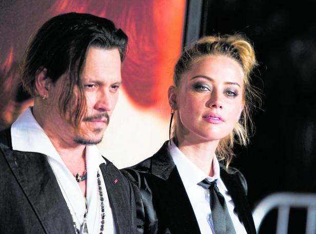 Johnny Depp und Amber Heard stehen nebeneinander vor einem rötlich beleuchteten Hintergrund.