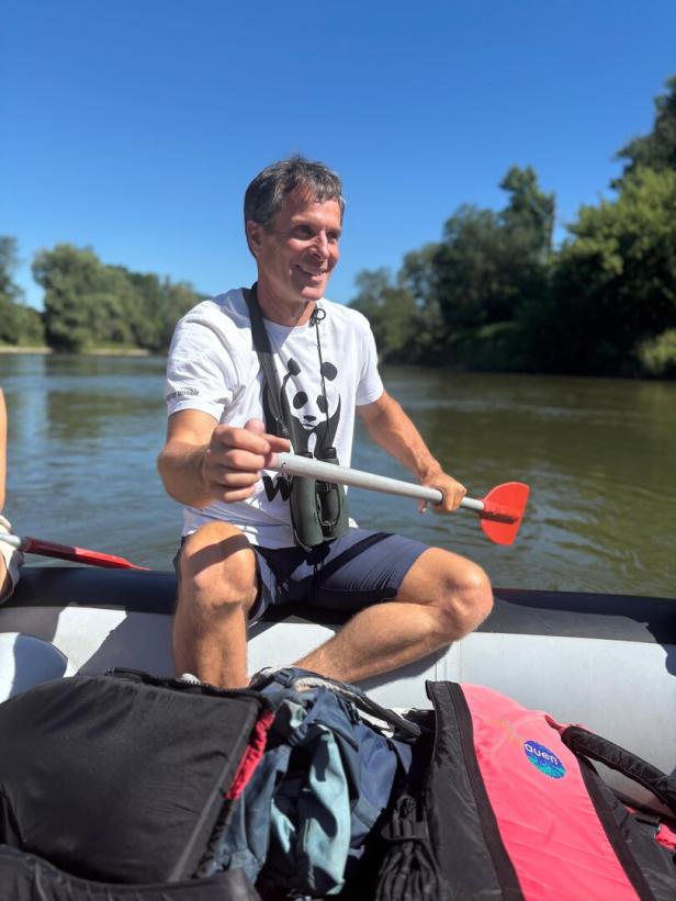 Ein Mann mit einem WWF-T-Shirt und Fernglas paddelt in einem Schlauchboot auf einem Fluss.