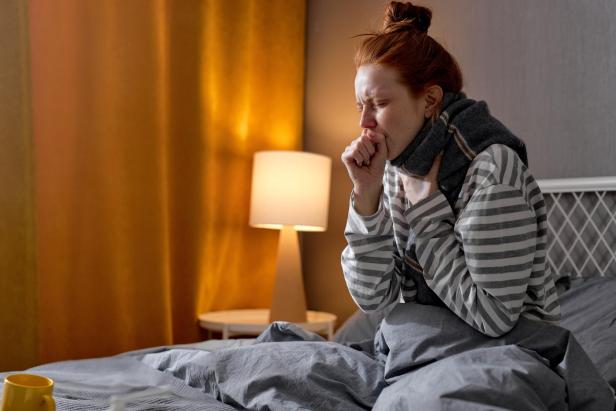 unhealthy week red-haired woman in scarf and sweater coughing, closing mouth with fist