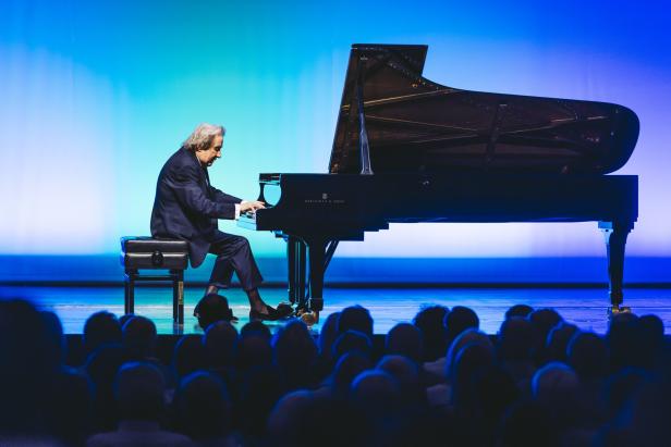 Rudolf Buchbinder spielt auf einem Flügel auf der Bühne vor Publikum.