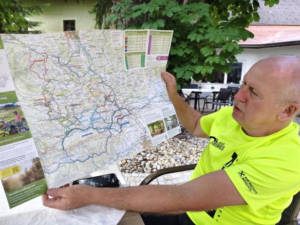 Mann im neonfarbenen Shirt betrachtet eine Wanderkarte im Freien.