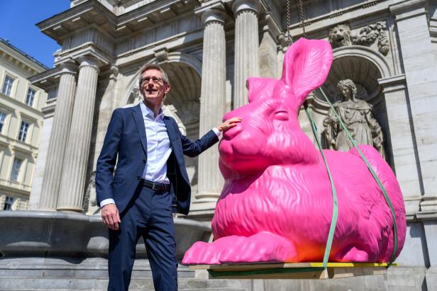Mann im Anzug neben einer grell pinken Kaninchen-Statue vor einer klassischen Säulenfassade.