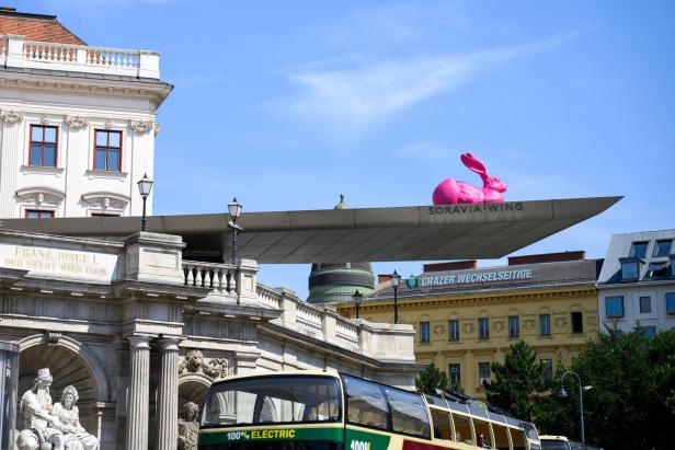 Marktplatz in Wien mit moderner Überdachung, pinkem Hasen auf dem Dach und historischem Gebäude im Hintergrund.