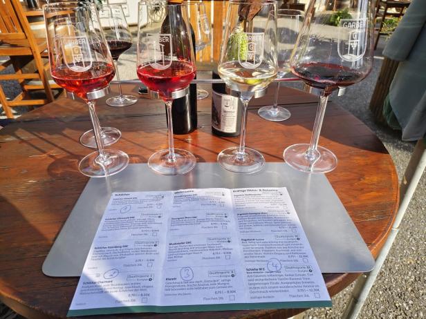 Mehrere Weingläser mit Rot-, Weiß- und Roséwein stehen auf einem Tisch mit Weinkarte.