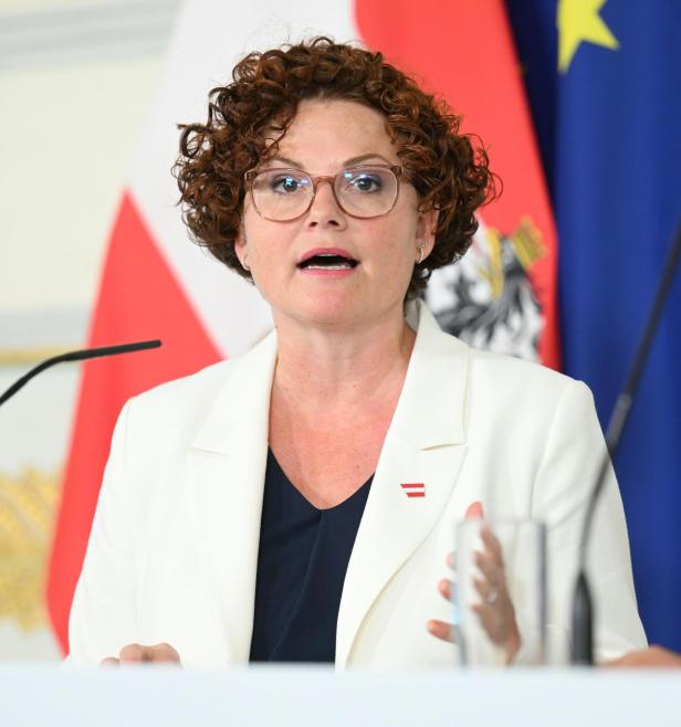 Eine Frau mit lockigen Haaren und Brille spricht am Pult vor Nationalflaggen.
