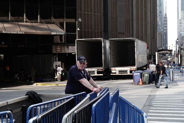 Ein Sicherheitsmitarbeiter lehnt an einer blauen Absperrung vor dem Madison Square Garden, während im Hintergrund zwei LKW-Auflieger stehen.