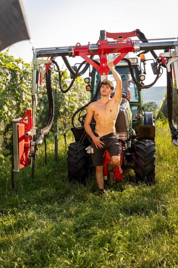 Ein oberkörperfreier Mann posiert vor einem Traktor