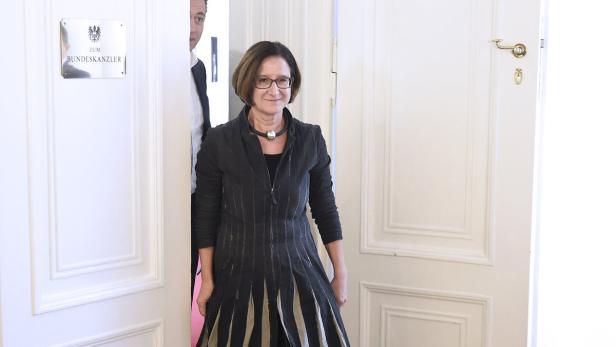 Eine Frau mit Brille betritt einen Raum; ein Schild weist auf das Büro des Bundeskanzlers hin.