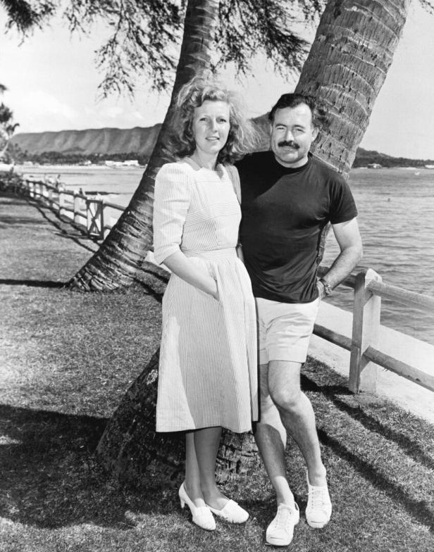 Ernest Hemingway steht mit seiner Frau Mary Welsh an einer Küste unter Palmen.
