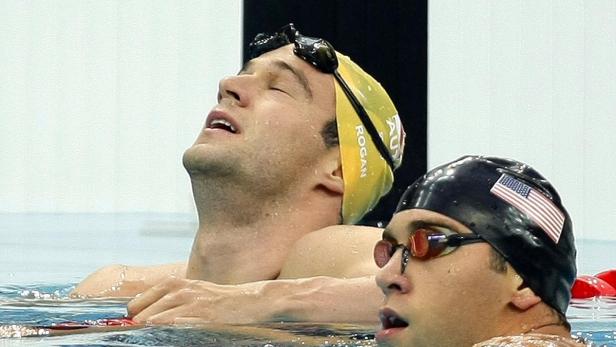Zwei Schwimmer im Wasser, einer mit einer Badekappe mit der US-Flagge.