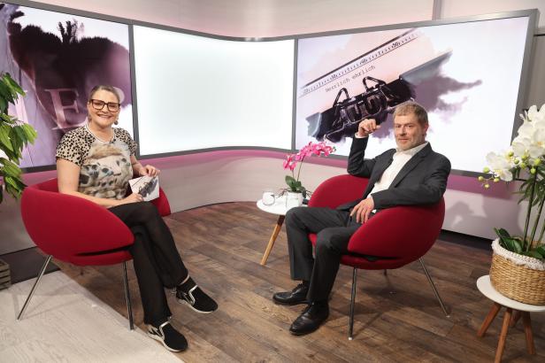 Eine Frau und ein Mann sitzen in einem Fernsehstudio in roten Sesseln vor Bildschirmen, auf denen der Schriftzug „Herrlich ehrlich“ zu sehen ist.