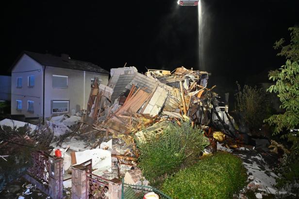 Nachtaufnahme: Ein Haus ist nach einem Einsturz zu einem Trümmerhaufen geworden, beleuchtet von einem Scheinwerfer.