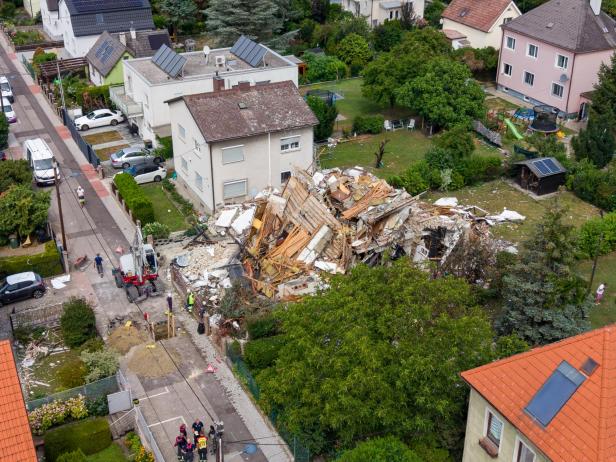 Ein eingestürztes Wohnhaus in einem Wohngebiet mit Einsatzkräften und einem Bagger vor Ort.