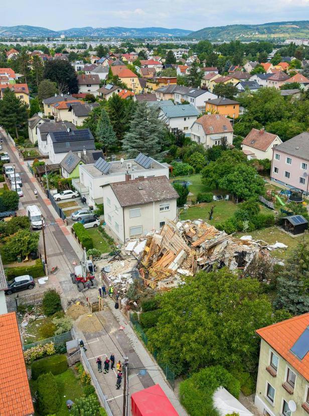 Luftaufnahme eines Wohnviertels mit zerstörtem Haus und Rettungskräften auf der Straße.