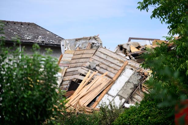 Eingestürztes Haus mit Trümmern aus Holz und Mauerwerk, umgeben von Bäumen.